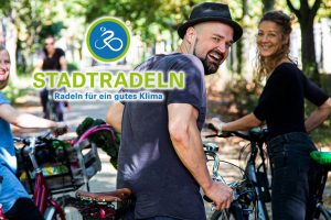 Drei lächelnde Radfahrer stehen auf einer Allee, das Logo der Aktion Stadtradeln ist im Foto sichtbar
