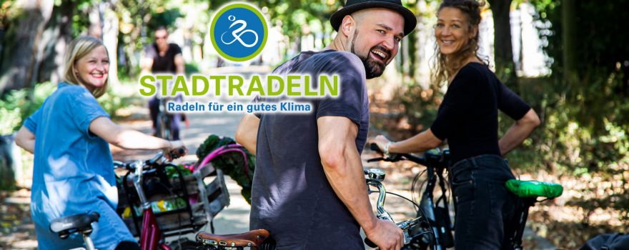 Drei lächelnde Radfahrer stehen auf einer Allee, das Logo der Aktion Stadtradeln ist im Foto sichtbar