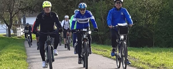 Eine Gruppe mit E-Bike-Fahrern fährt auf einem asphaltierten Feldweg